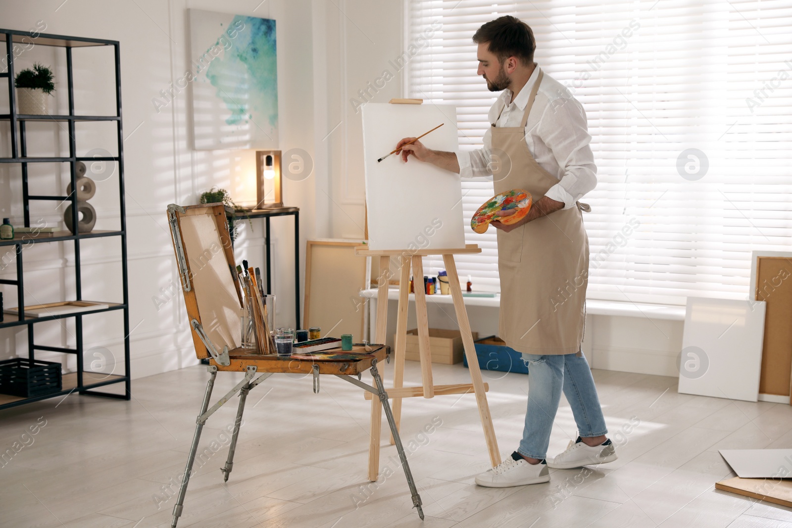 Young man painting on easel with brush in artist studio Photo of Young man painting on easel with brush in artist studio