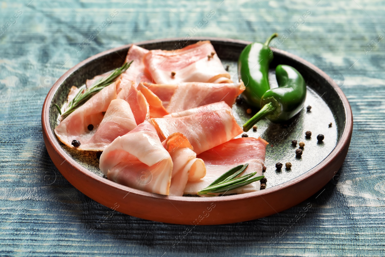 Plate with raw bacon rashers and peppers on wooden background Photo of Plate with raw bacon rashers and peppers on wooden background