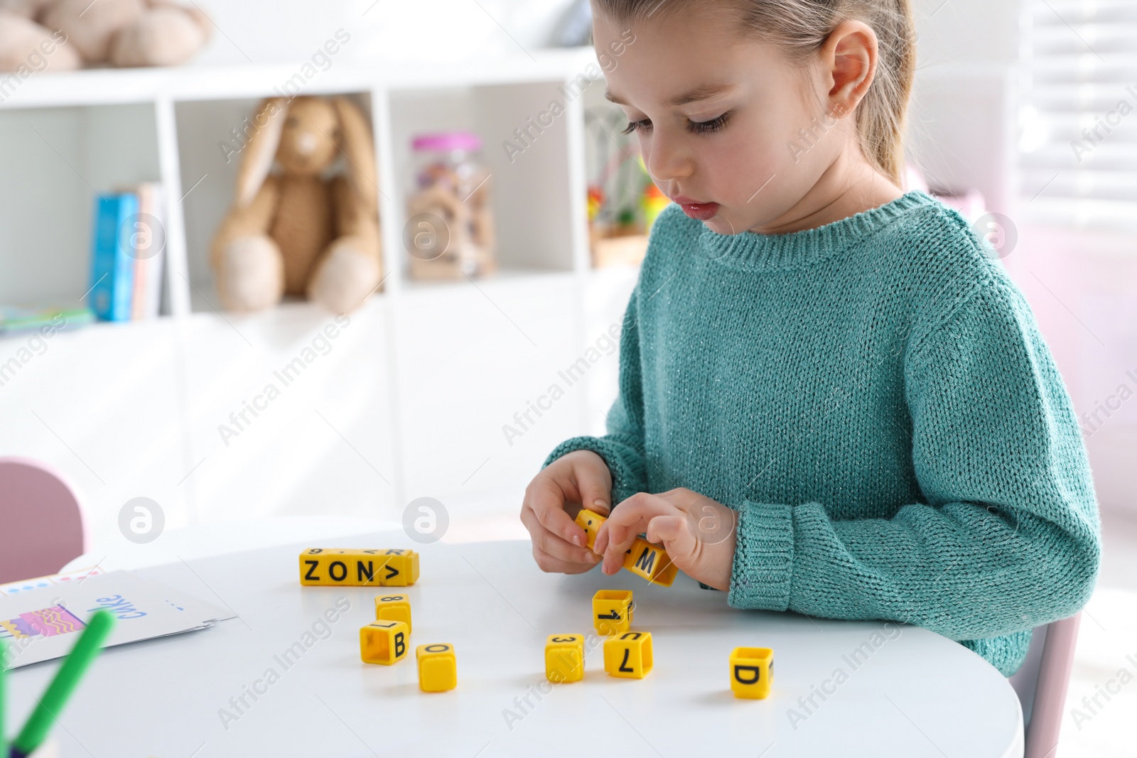 Little girl assembling word with yellow bricks in classroom at English lesson Photo of Little girl assembling word with yellow bricks in classroom at English lesson