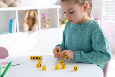Little girl assembling word with yellow bricks in classroom at English lesson Photo of Little girl assembling word with yellow bricks in classroom at English lesson