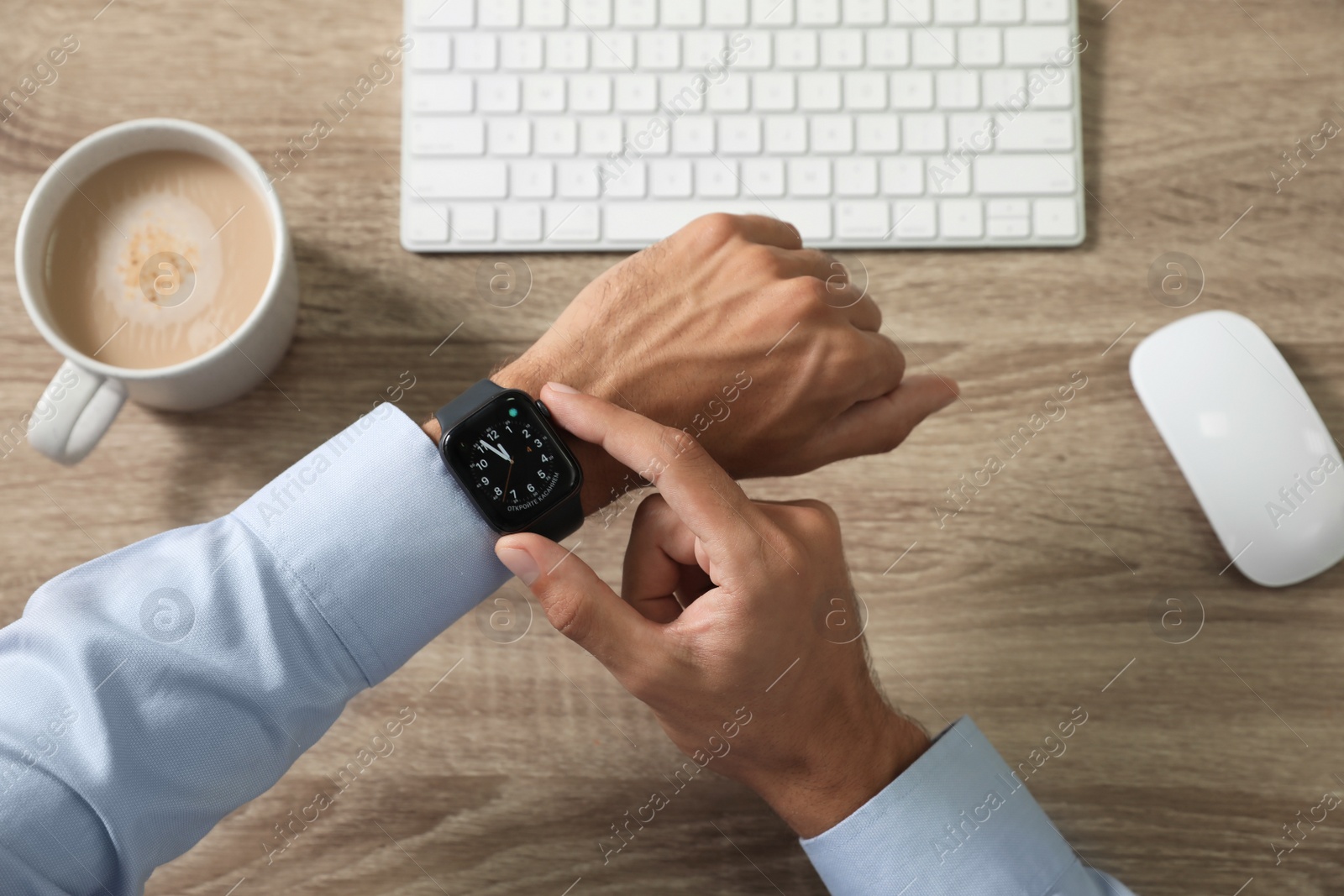 MYKOLAIV, UKRAINE - OCTOBER 04, 2019: Man using Apple Watch to check time at wooden table, top view Image of MYKOLAIV, UKRAINE - OCTOBER 04, 2019: Man using Apple Watch to check time at wooden table, top view
