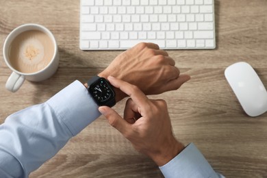 MYKOLAIV, UKRAINE - OCTOBER 04, 2019: Man using Apple Watch to check time at wooden table, top view Image of MYKOLAIV, UKRAINE - OCTOBER 04, 2019: Man using Apple Watch to check time at wooden table, top view