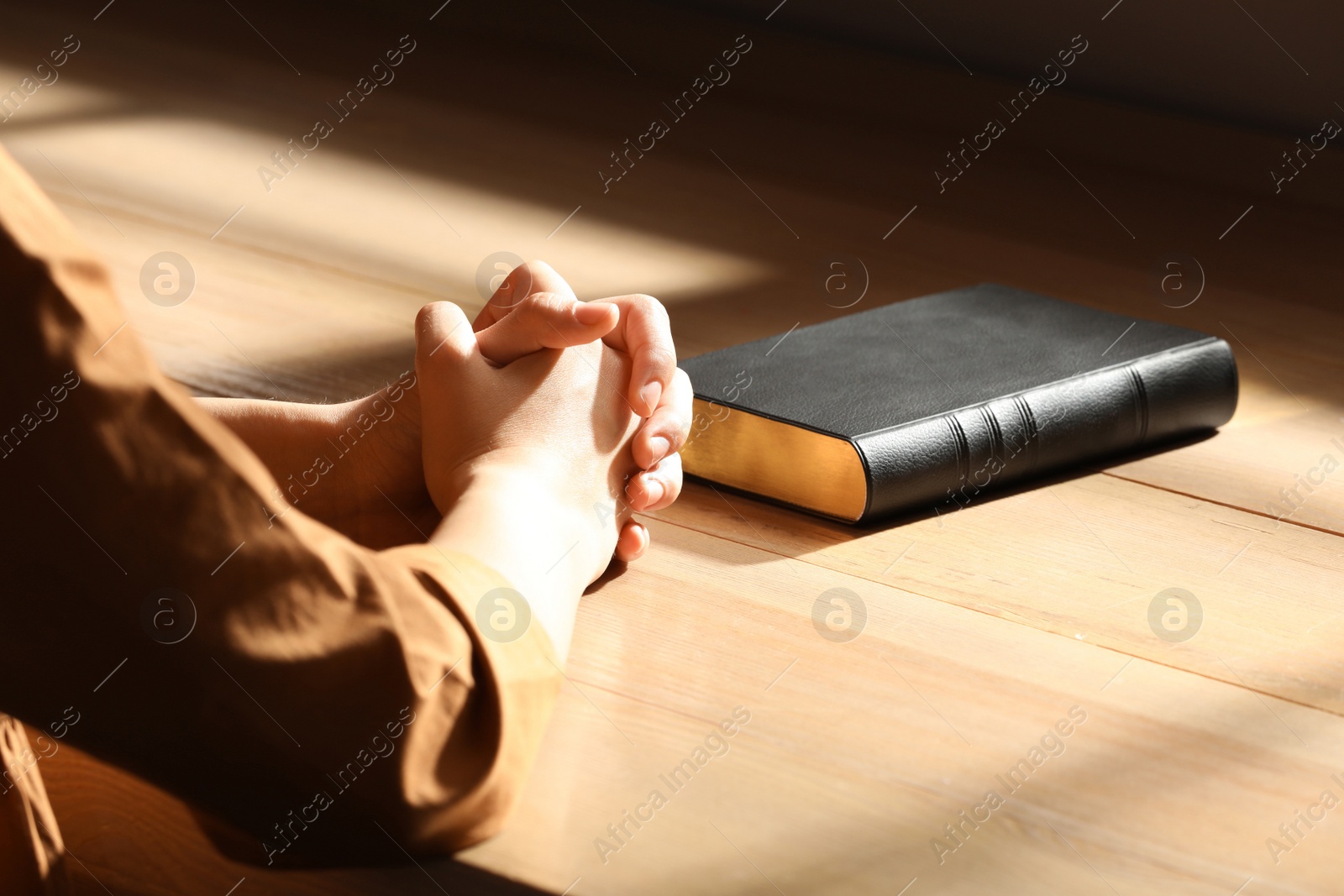 Photo of Religious woman praying over Bible indoors, closeup