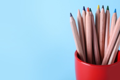 Colorful pencils in cup on light blue background, closeup. Space for text Photo of Colorful pencils in cup on light blue background, closeup. Space for text