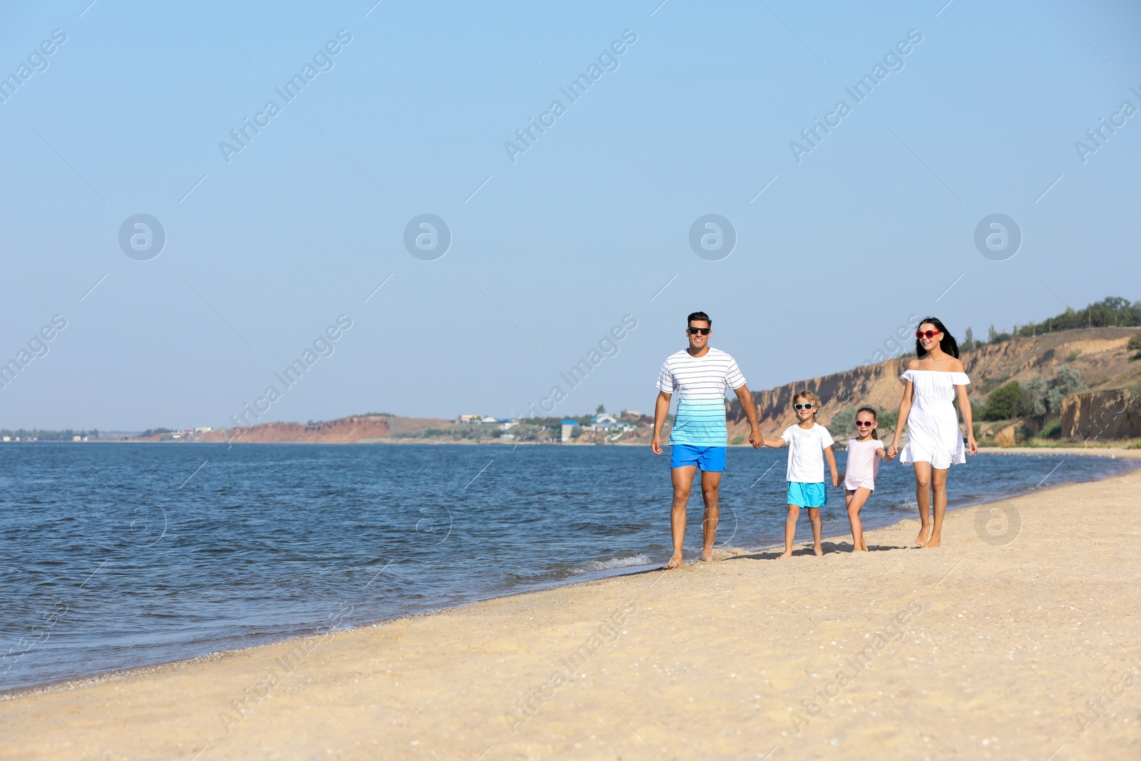 Happy family walking on sandy beach near sea, space for text. Summer holidays Photo of Happy family walking on sandy beach near sea, space for text. Summer holidays