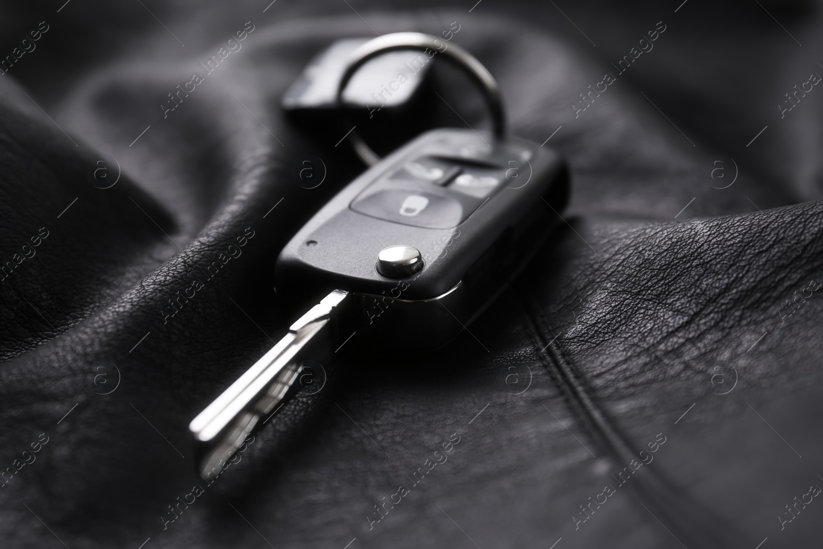 Photo of Modern car flip key with trinket on black leather, closeup