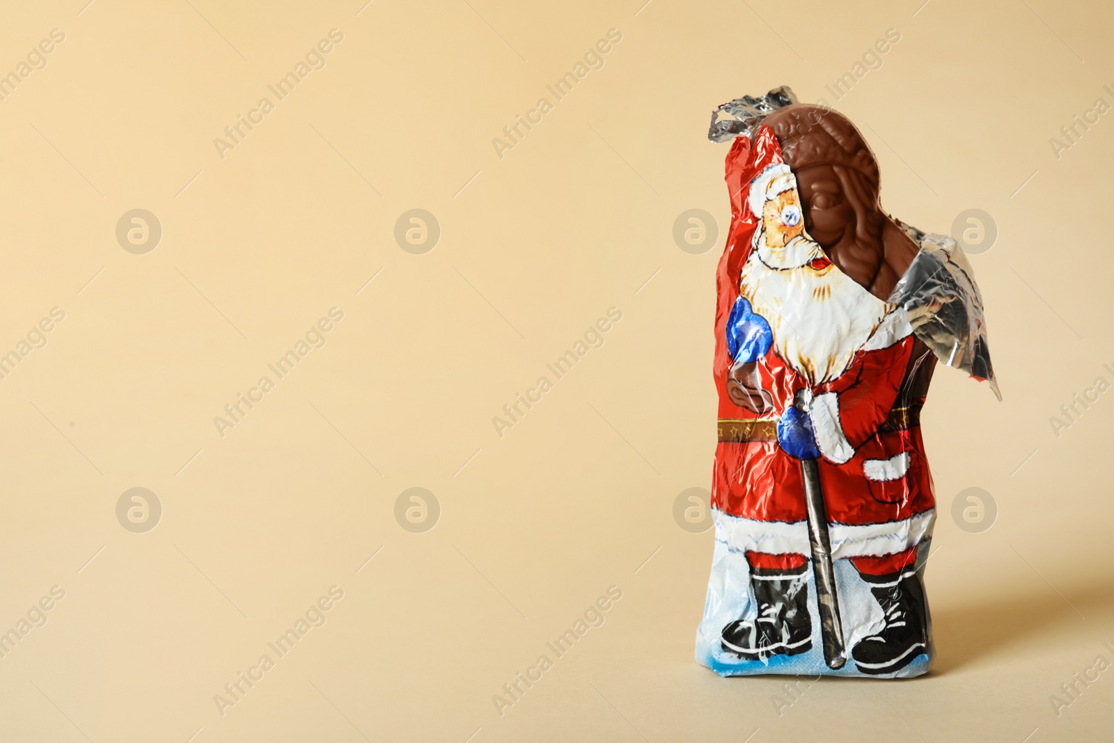Sweet chocolate Santa Claus candy in slightly open foil wrapper on beige background, space for text Photo of Sweet chocolate Santa Claus candy in slightly open foil wrapper on beige background, space for text