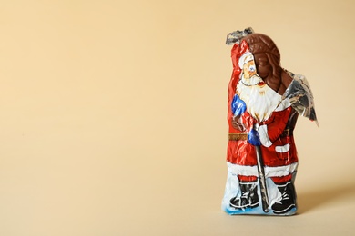 Sweet chocolate Santa Claus candy in slightly open foil wrapper on beige background, space for text Photo of Sweet chocolate Santa Claus candy in slightly open foil wrapper on beige background, space for text