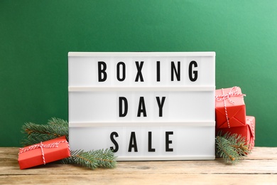 Composition with Boxing Day Sale sign and Christmas gifts on wooden table against green background Photo of Composition with Boxing Day Sale sign and Christmas gifts on wooden table against green background
