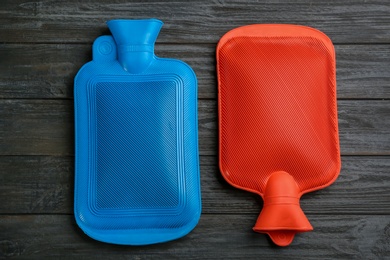Rubber hot water bottles on black wooden background, flat lay Photo of Rubber hot water bottles on black wooden background, flat lay