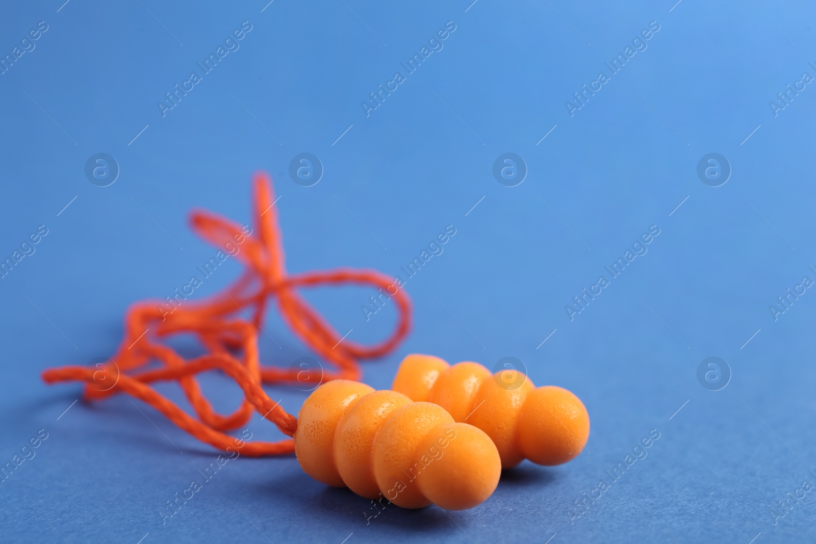 Pair of orange ear plugs with cord on blue background, closeup. Space for text Photo of Pair of orange ear plugs with cord on blue background, closeup. Space for text