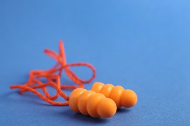 Photo of Pair of orange ear plugs with cord on blue background, closeup. Space for text