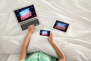 Woman using tablet, mobile phone and laptop with Black Friday announcement while lying in bed, above view Photo of Woman using tablet, mobile phone and laptop with Black Friday announcement while lying in bed, above view
