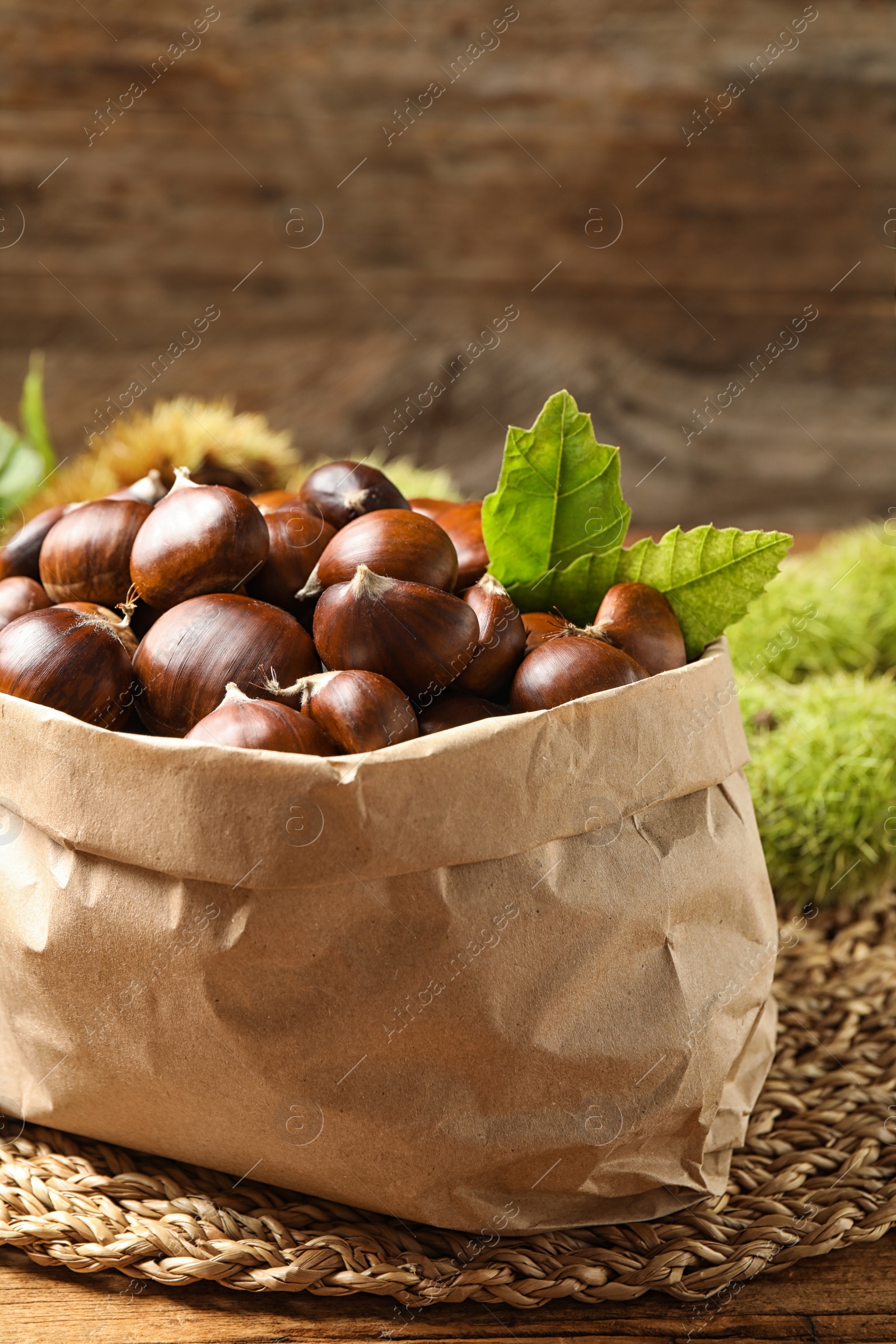 Photo of Fresh sweet edible chestnuts in paper bag on wooden table, closeup
