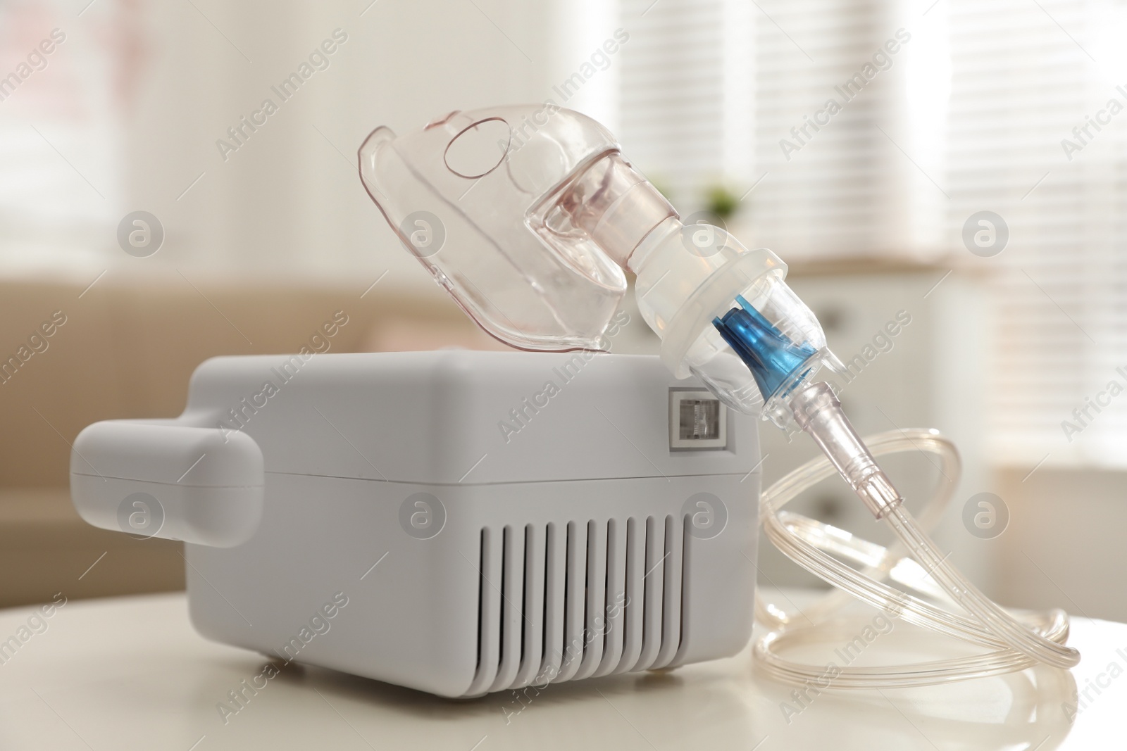 Modern nebulizer with face mask on white table indoors. Inhalation equipment Photo of Modern nebulizer with face mask on white table indoors. Inhalation equipment