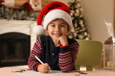 Cute child writing letter to Santa Claus at table indoors. Christmas tradition Photo of Cute child writing letter to Santa Claus at table indoors. Christmas tradition