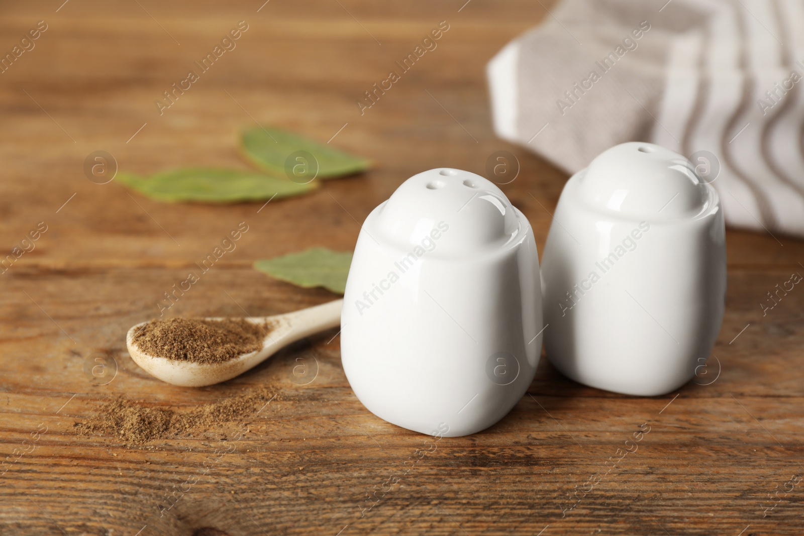 White ceramic salt and pepper shakers with spoon on wooden table, closeup Photo of White ceramic salt and pepper shakers with spoon on wooden table, closeup