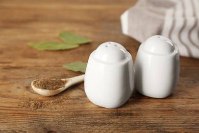 White ceramic salt and pepper shakers with spoon on wooden table, closeup Photo of White ceramic salt and pepper shakers with spoon on wooden table, closeup
