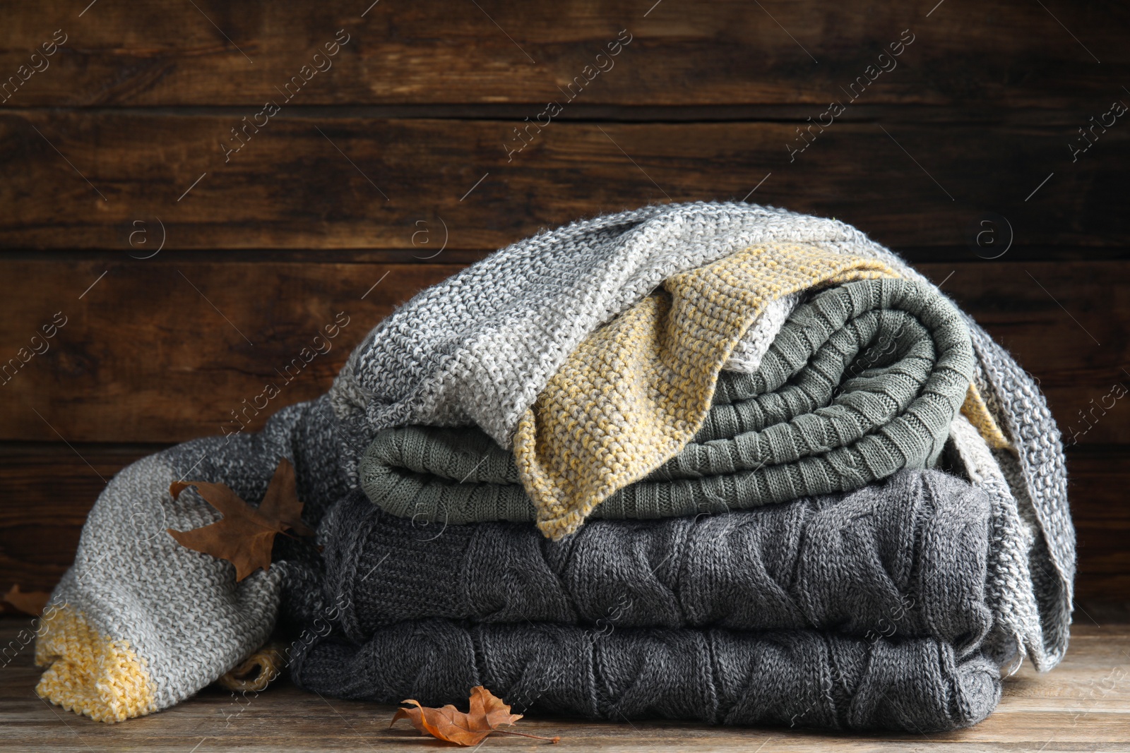 Stack of knitted plaids with dry leaves on wooden table, closeup Photo of Stack of knitted plaids with dry leaves on wooden table, closeup