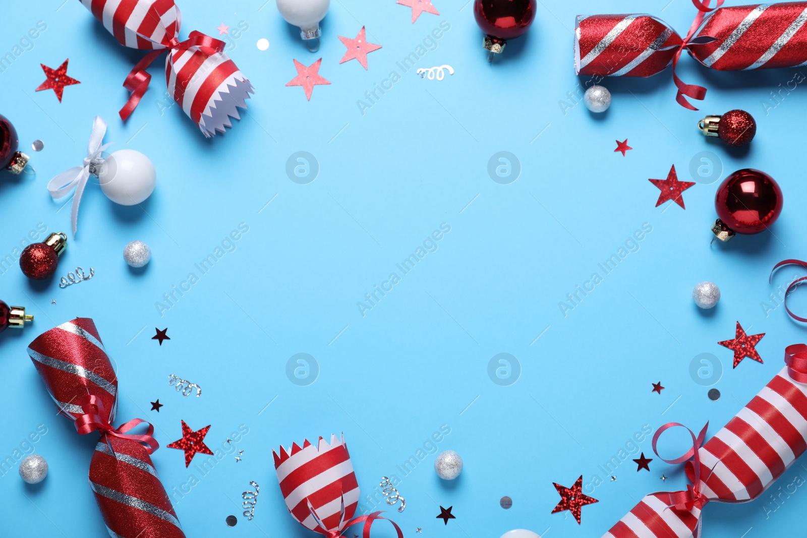Frame of Christmas crackers and decorations on light blue background, top view with space for text Photo of Frame of Christmas crackers and decorations on light blue background, top view with space for text