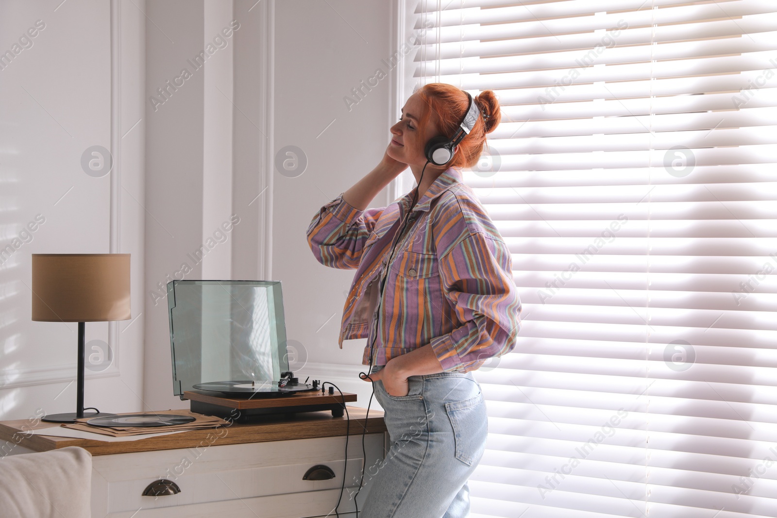 Photo of Young woman listening to music with turntable at home