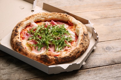 Tasty pizza with meat and arugula in cardboard box on wooden table Photo of Tasty pizza with meat and arugula in cardboard box on wooden table