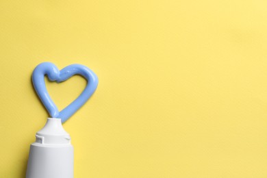 Blank tube and heart made with toothpaste on yellow background, flat lay. Space for text Photo of Blank tube and heart made with toothpaste on yellow background, flat lay. Space for text