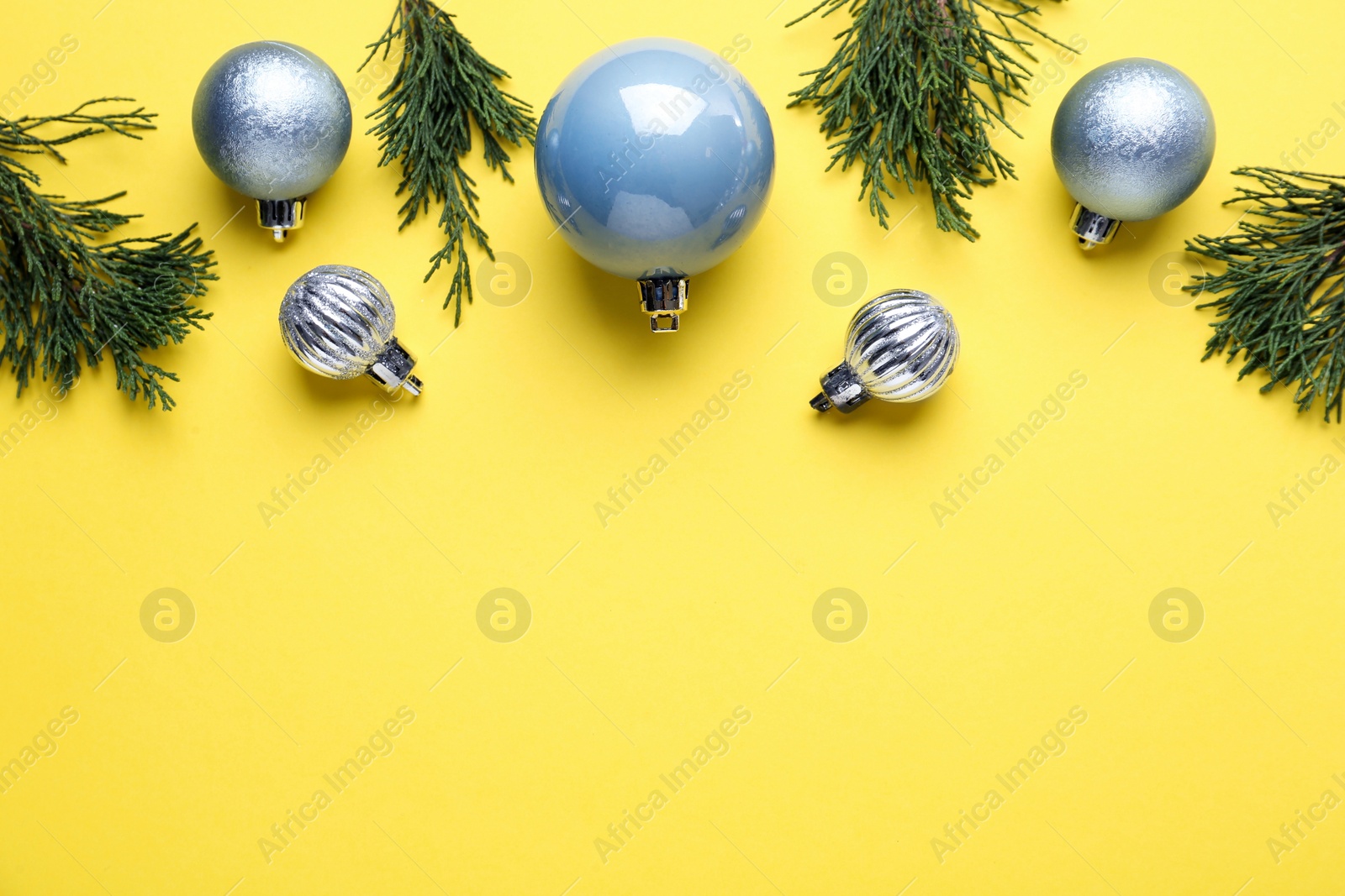 Beautiful blue Christmas balls and fir branches on yellow background, flat lay. Space for text Photo of Beautiful blue Christmas balls and fir branches on yellow background, flat lay. Space for text