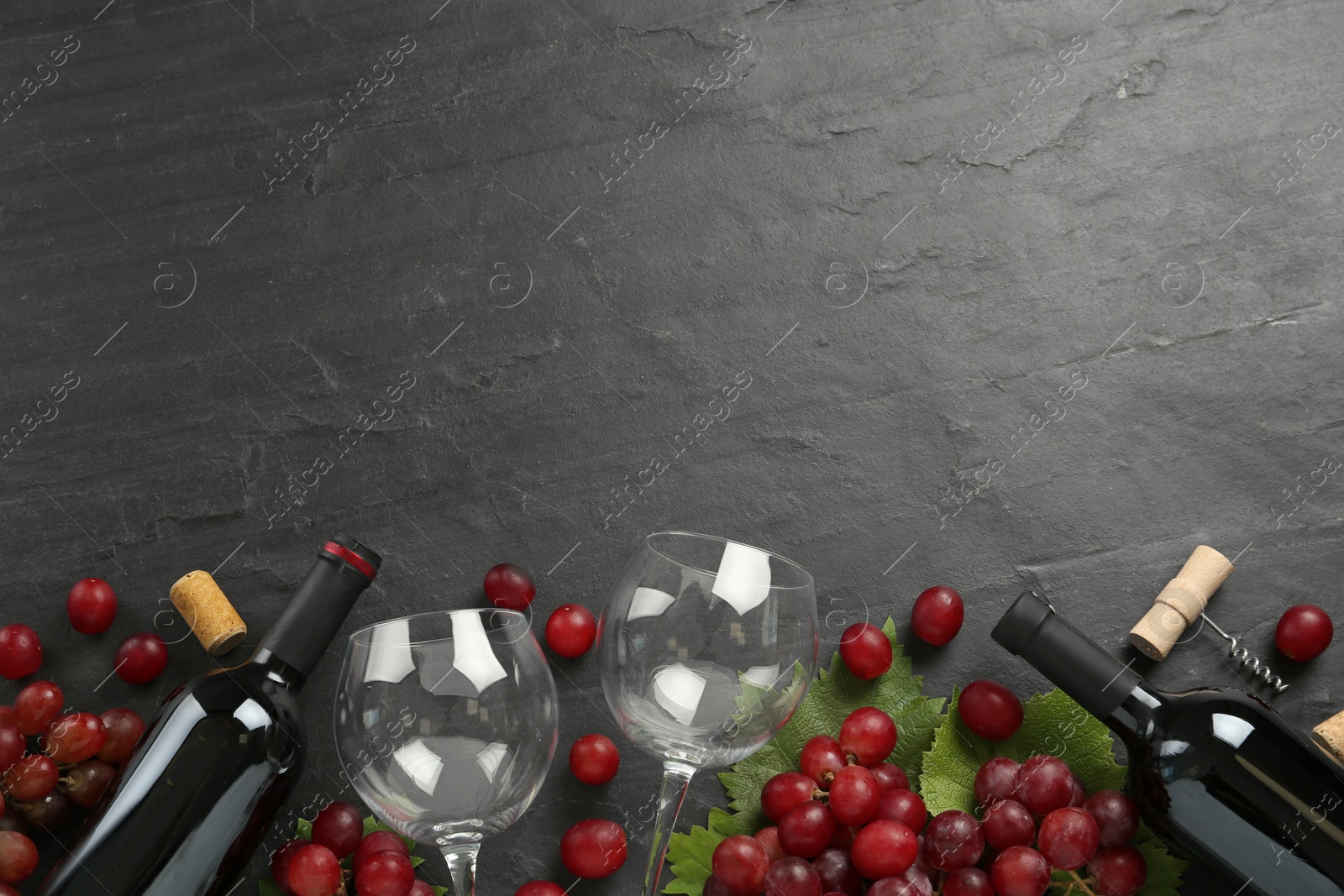 Bottles of red wine, glasses and grapes on black table, flat lay. Space for text Photo of Bottles of red wine, glasses and grapes on black table, flat lay. Space for text