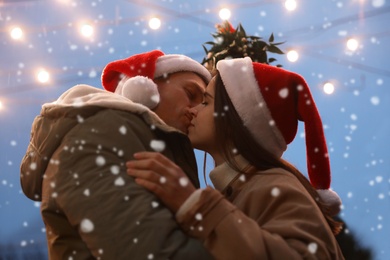 Happy couple kissing under mistletoe bunch outdoors in snowy evening, low angle view Photo of Happy couple kissing under mistletoe bunch outdoors in snowy evening, low angle view