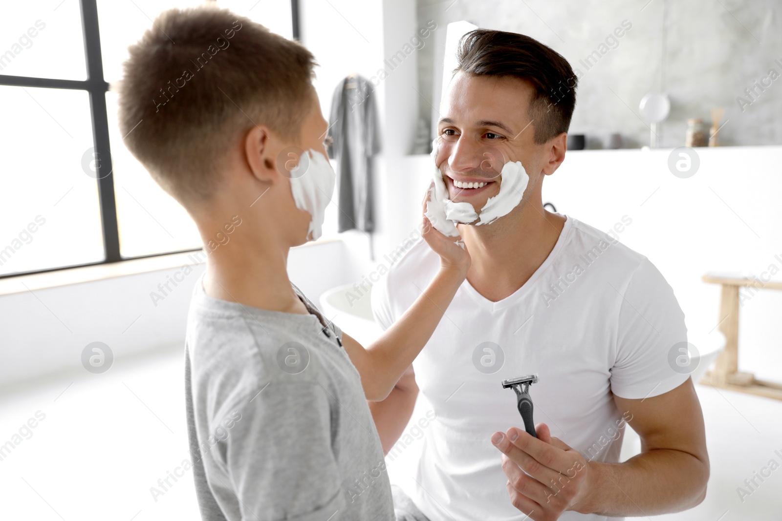 Son applying shaving foam onto father's face in bathroom Photo of Son applying shaving foam onto father's face in bathroom