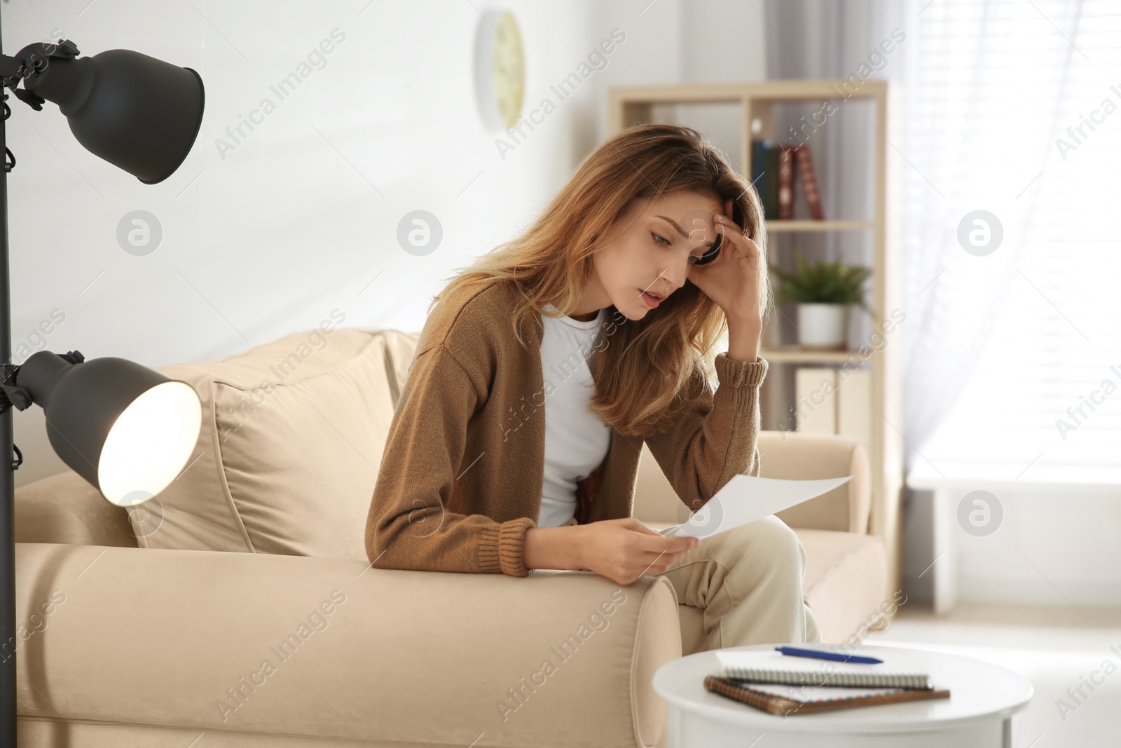Worried woman reading letter on sofa at home Photo of Worried woman reading letter on sofa at home