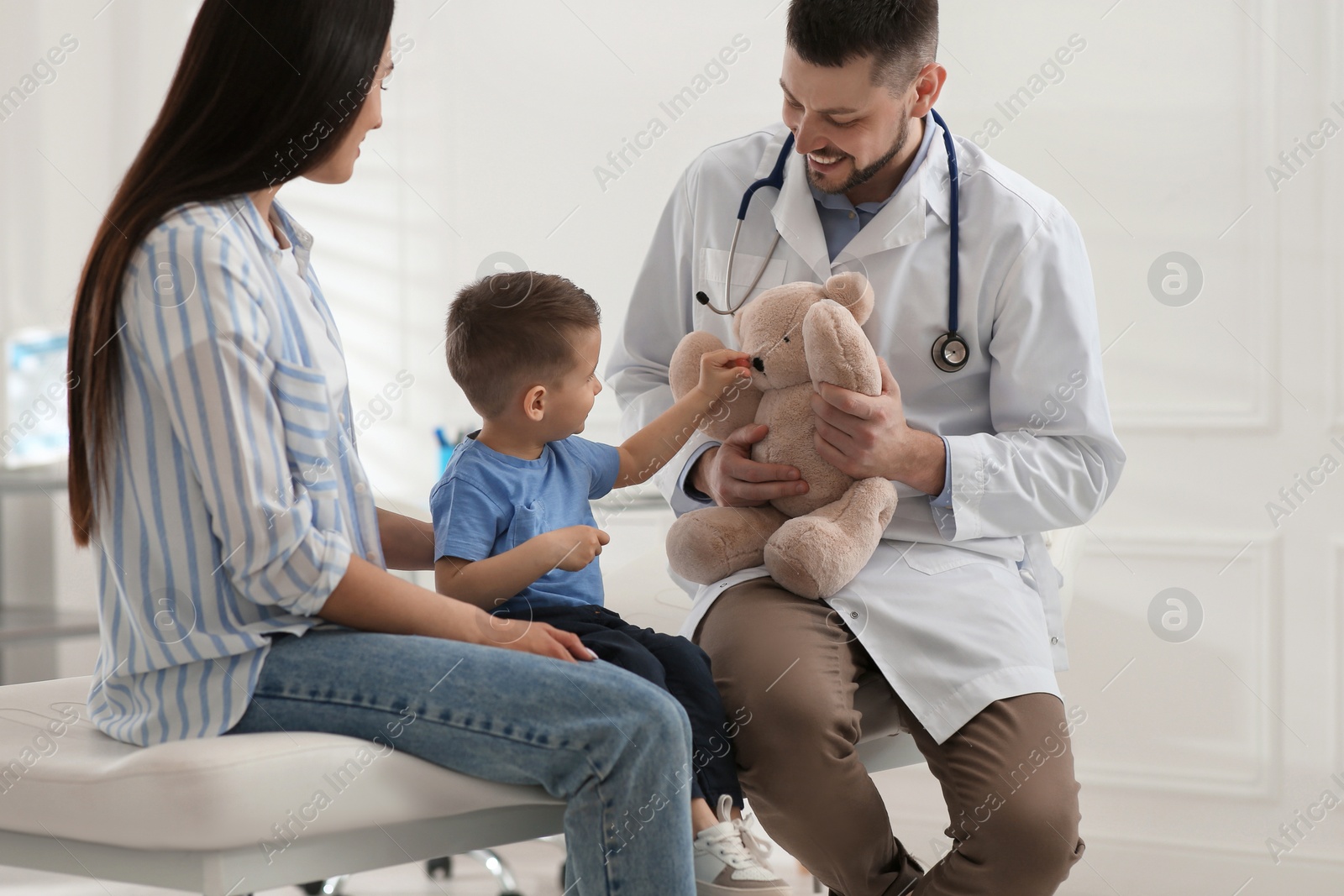 Photo of Mother and son visiting pediatrician in hospital. Doctor playing with little boy