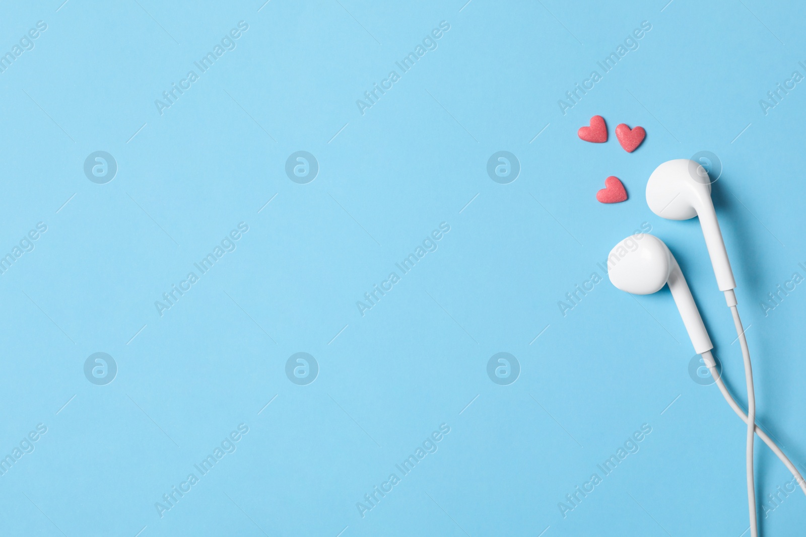 Modern earphones and pink heart shaped sprinkles on light blue background, flat lay with space for text. Listening love music songs Photo of Modern earphones and pink heart shaped sprinkles on light blue background, flat lay with space for text. Listening love music songs