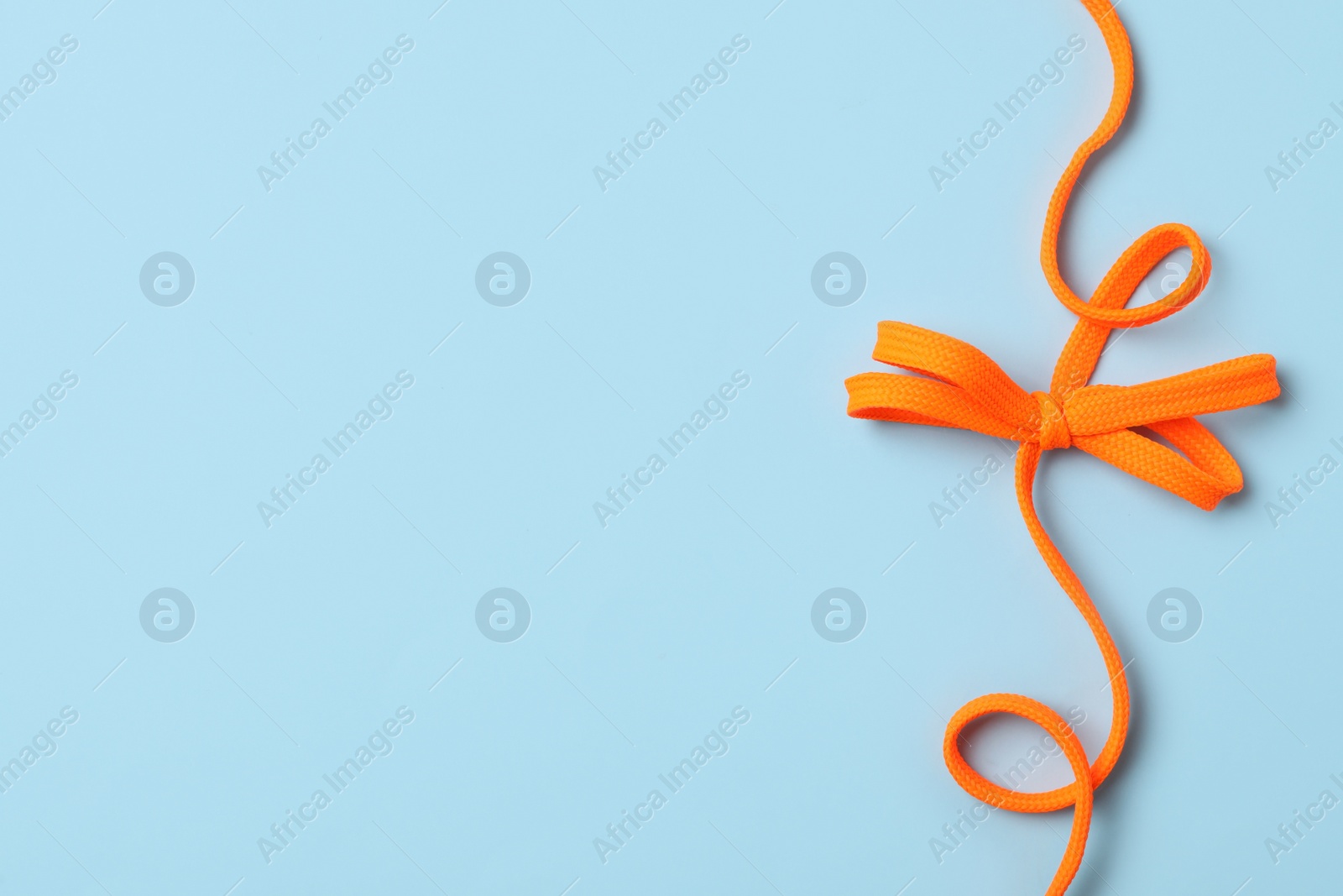 Orange shoelace on light blue background, top view. Space for text Photo of Orange shoelace on light blue background, top view. Space for text
