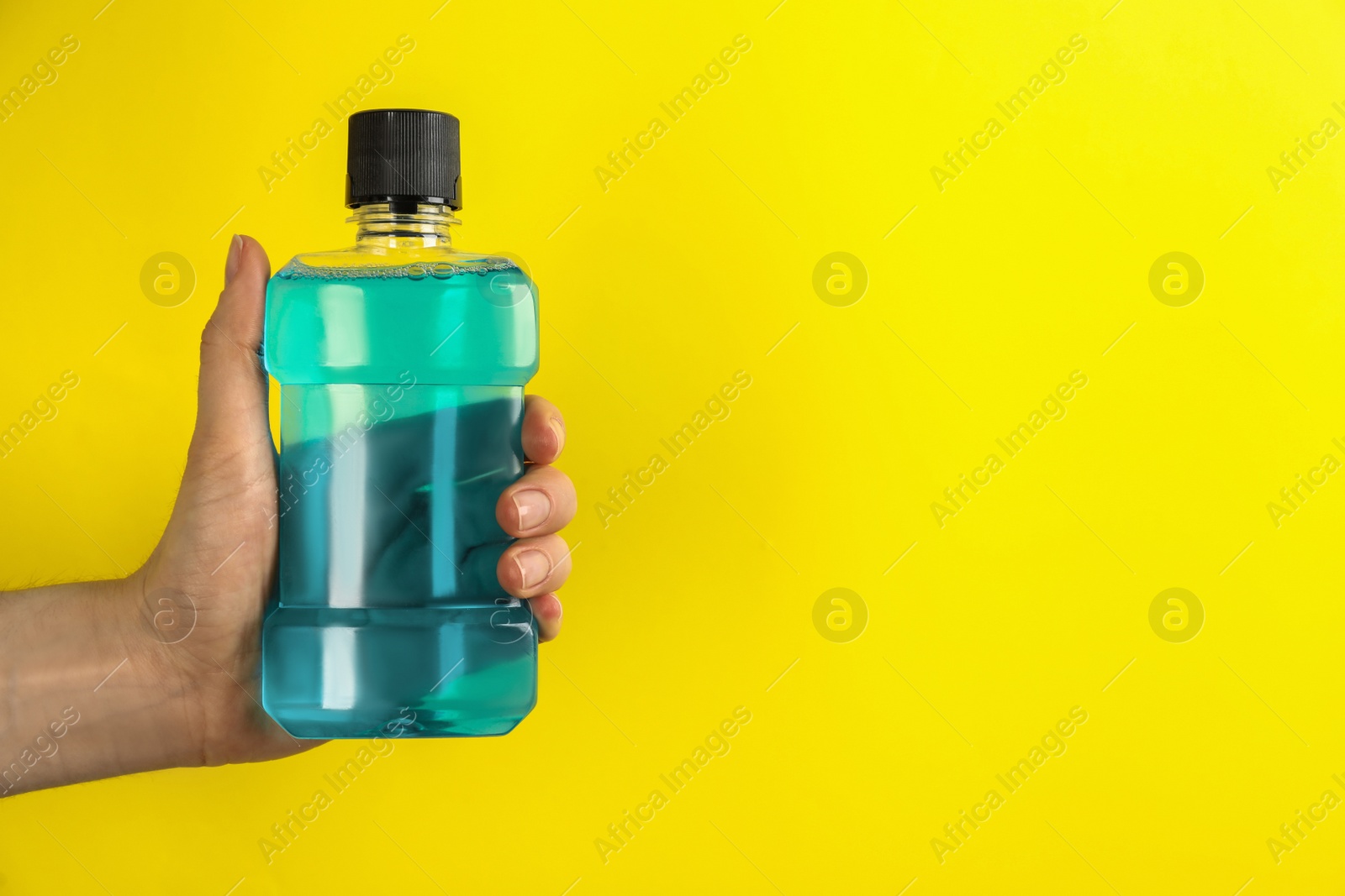 Woman holding bottle with mouthwash on yellow background, closeup. Space for text Photo of Woman holding bottle with mouthwash on yellow background, closeup. Space for text