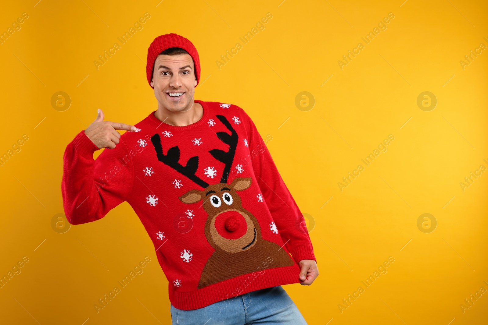 Happy man in hat showing his Christmas sweater on yellow background Photo of Happy man in hat showing his Christmas sweater on yellow background