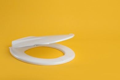 New white plastic toilet seat on yellow background, space for text Photo of New white plastic toilet seat on yellow background, space for text