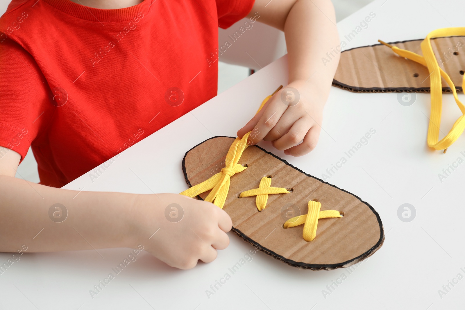 Little boy tying shoe lace using training cardboard template at white table, closeup Photo of Little boy tying shoe lace using training cardboard template at white table, closeup