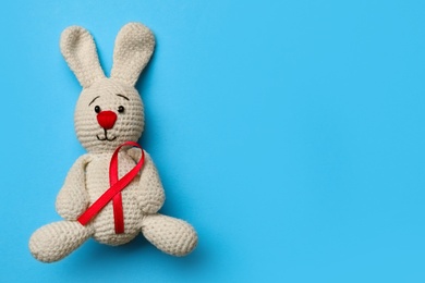 Cute knitted toy bunny with red ribbon on blue background, top view and space for text. AIDS disease awareness Photo of Cute knitted toy bunny with red ribbon on blue background, top view and space for text. AIDS disease awareness