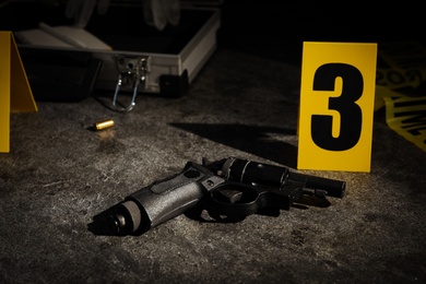 Shell casing, gun and crime scene marker on grey stone table Photo of Shell casing, gun and crime scene marker on grey stone table