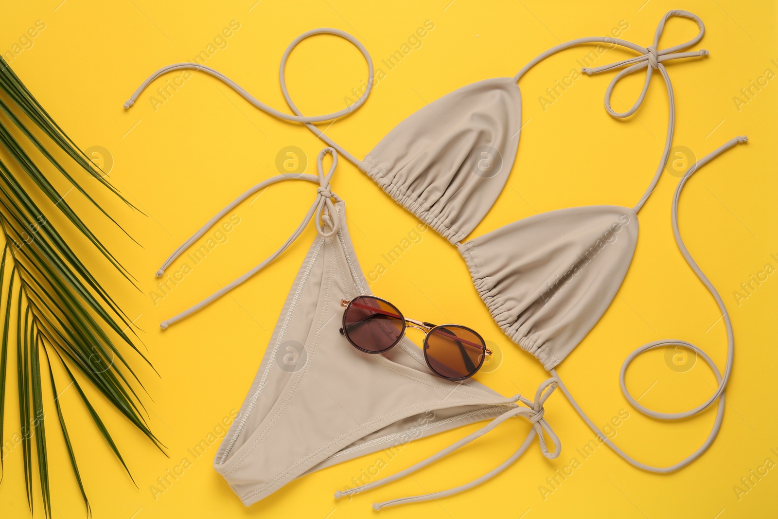 Stylish beige bikini, sunglasses and leaf on yellow background, flat lay Photo of Stylish beige bikini, sunglasses and leaf on yellow background, flat lay