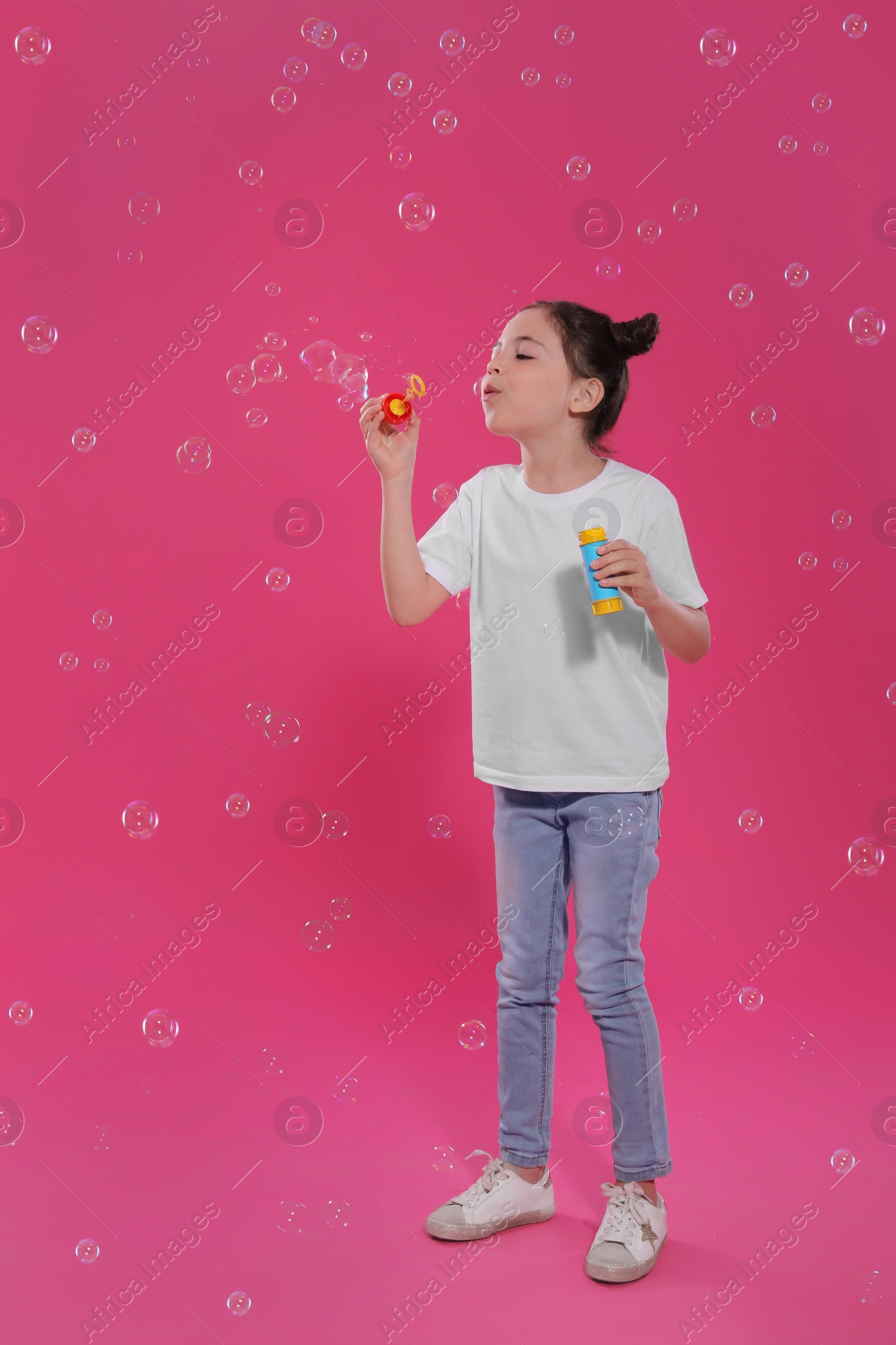 Little girl blowing soap bubbles on pink background Photo of Little girl blowing soap bubbles on pink background