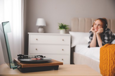 Young woman listening to music in bedroom, focus on turntable Photo of Young woman listening to music in bedroom, focus on turntable