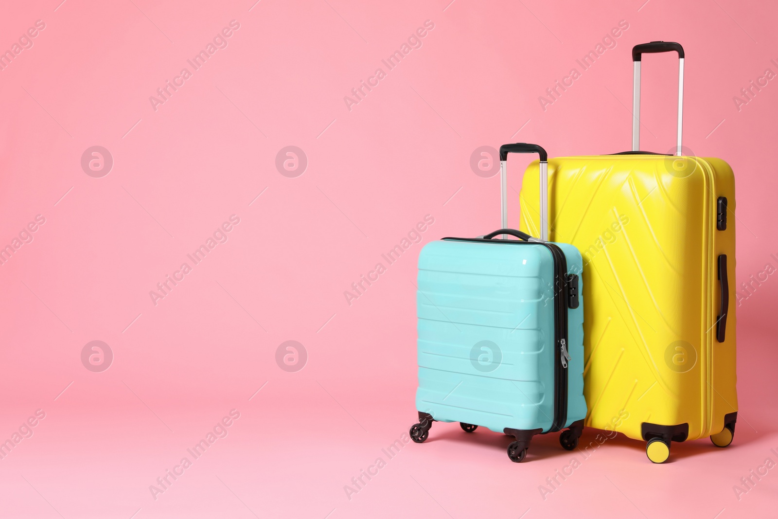 Photo of Stylish yellow and turquoise suitcases on pink background. Space for text