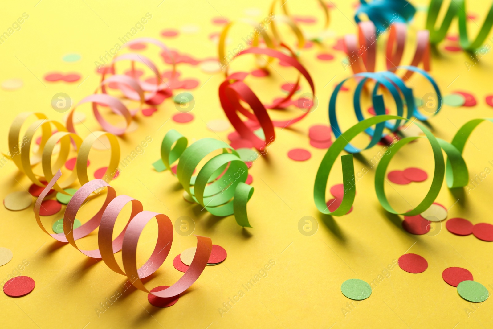 Colorful serpentine streamers and confetti on yellow background Photo of Colorful serpentine streamers and confetti on yellow background