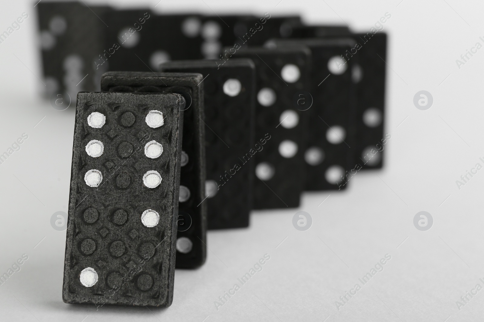 Black domino tiles falling on white background. Space for text Photo of Black domino tiles falling on white background. Space for text