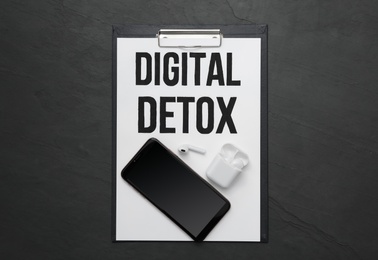 Clipboard with phrase DIGITAL DETOX, smartphone and earphones on black stone table, flat lay Photo of Clipboard with phrase DIGITAL DETOX, smartphone and earphones on black stone table, flat lay