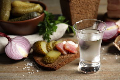 Photo of Cold Russian vodka with snacks on wooden table, closeup