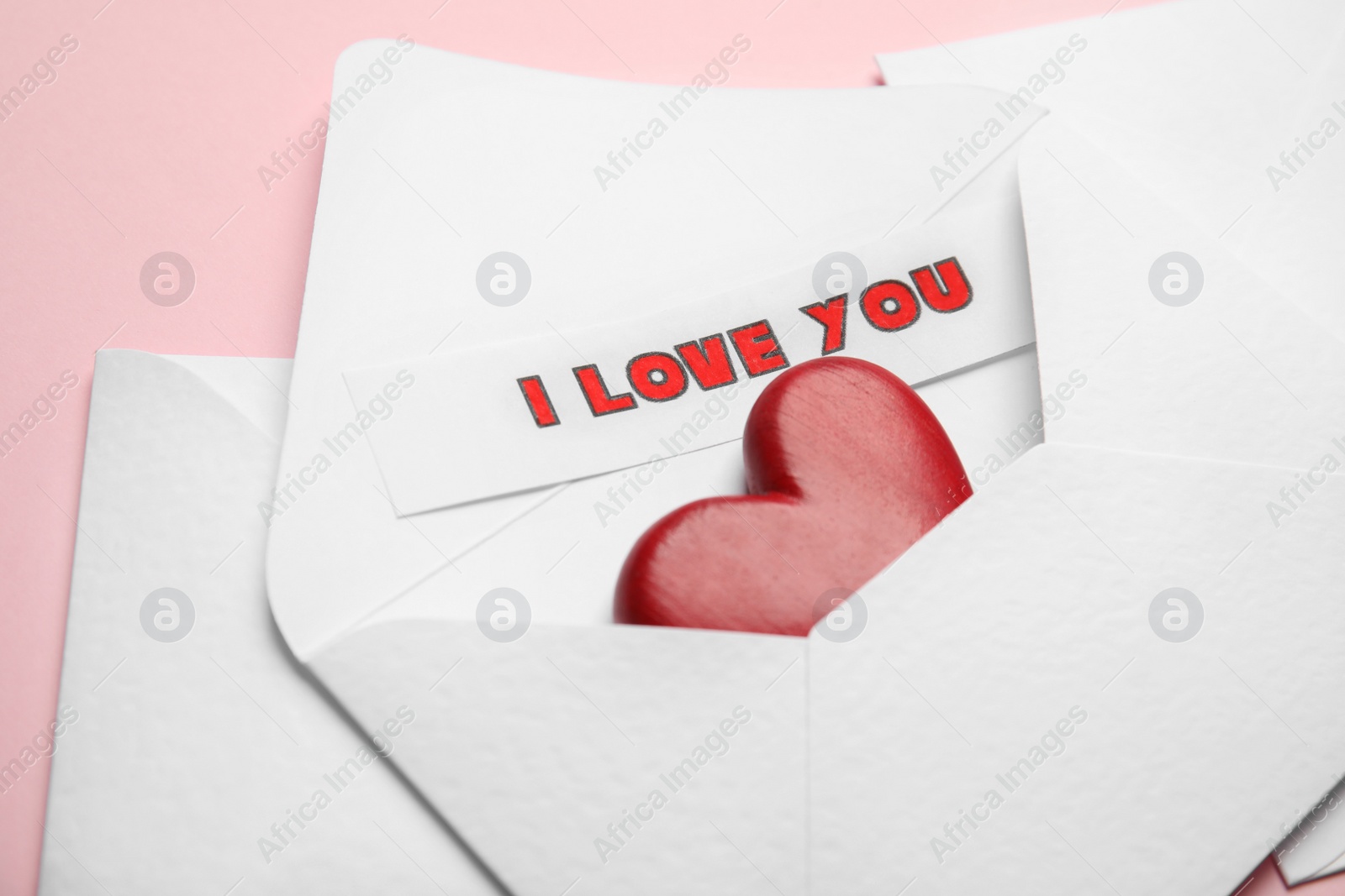 Sheet of paper with phrase I Love You and decorative heart in envelope on pink background, closeup Photo of Sheet of paper with phrase I Love You and decorative heart in envelope on pink background, closeup
